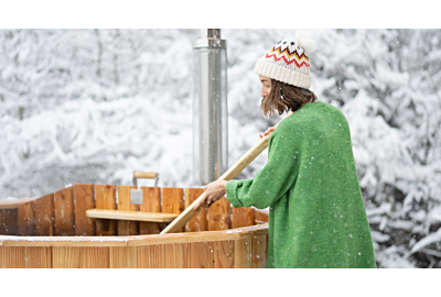 kobieta mieszajaca gorącą wode w bali ogorodowej ustawionej w osniezonym ogrodzie przy lesie