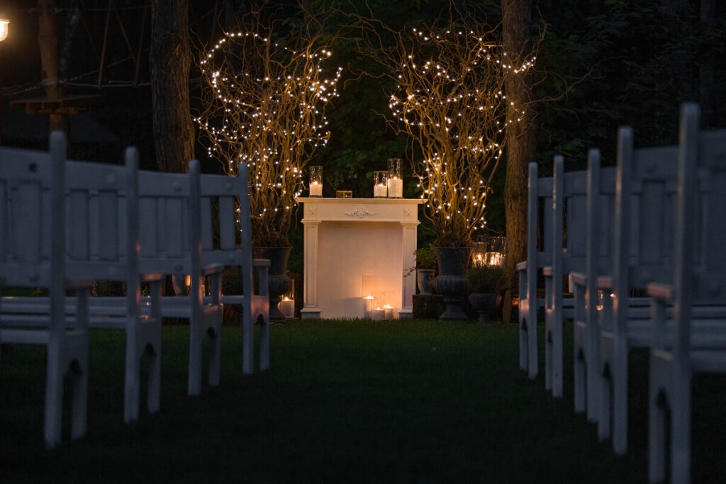 Biokominek w ogrodzie na ślubnej aranżacji z białych krzesełek i nastrojowych lampek