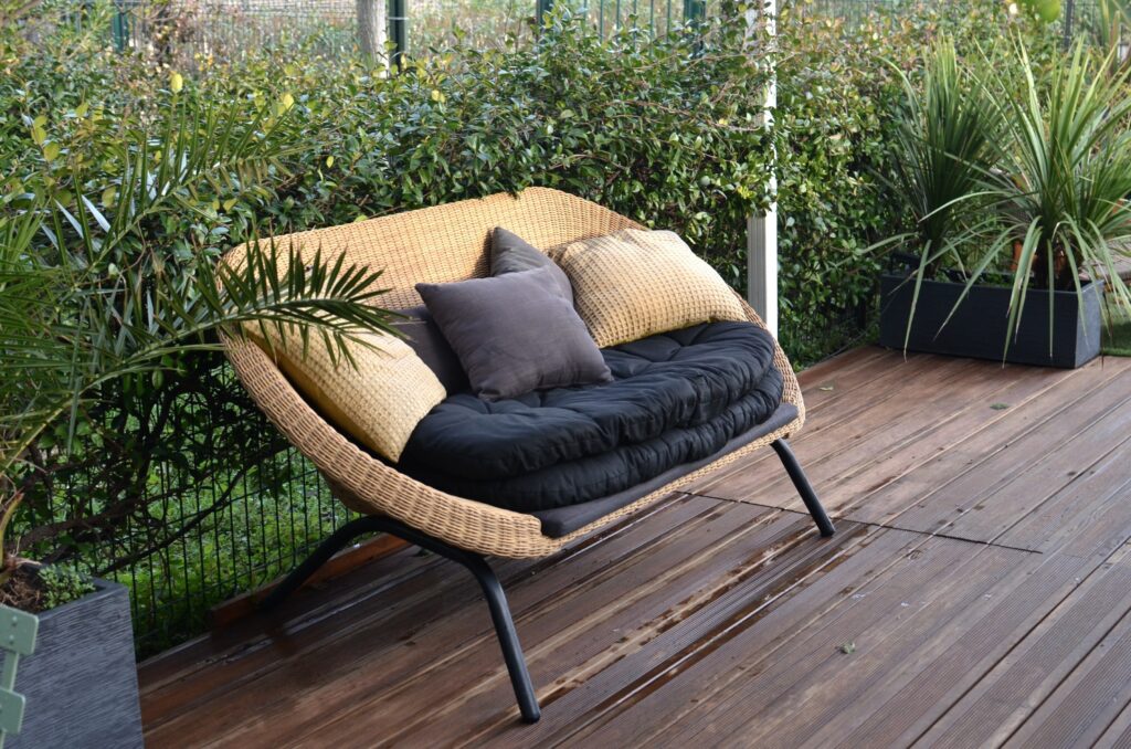technorattanowa sofa i stylowe dodatki na balkonie w bloku z drewnianym podestem w kolorze ciemnego brązu 
