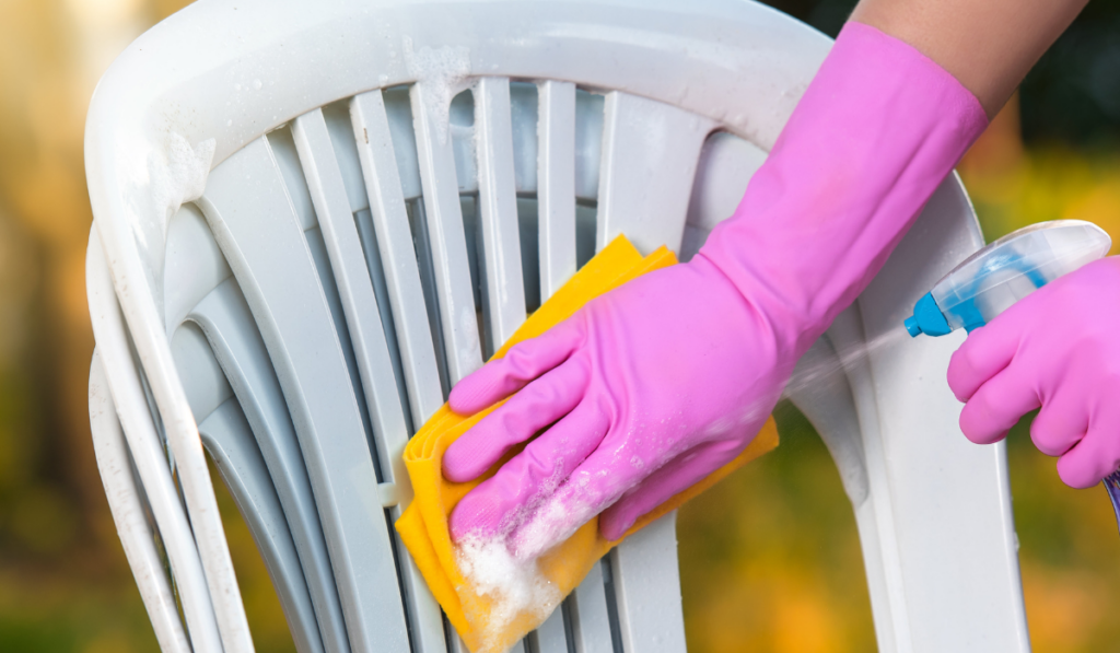 kobieta w różowych rękawiczkach i żółtą ściereczką czyszcząca meble z tworzywa płynem do mycia 