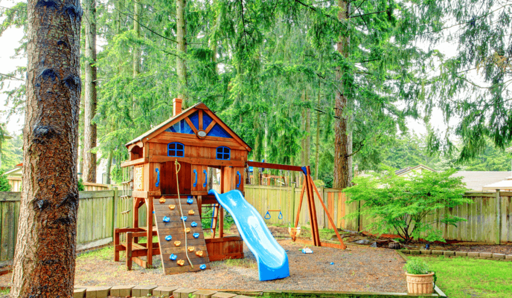 atrakcje dla dzieci z drewniany domkiem i niebieską zjeżdżalnią w domowym ogrodzie 