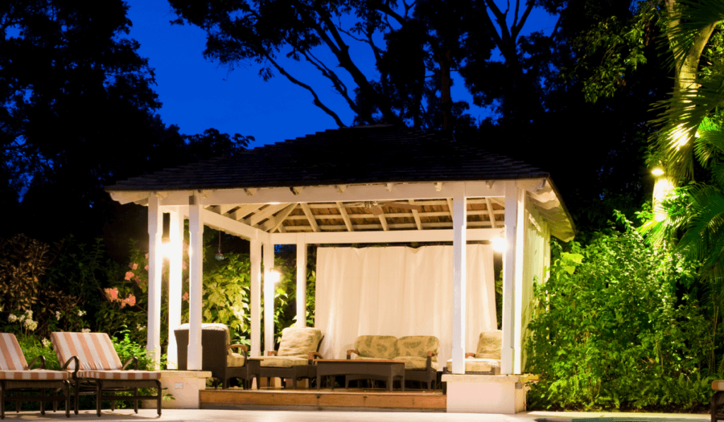 altana ogrodowa pomalowana na biało ustawiona na działce z meblami wypoczynkowymi i nastrojowym oświetleniem