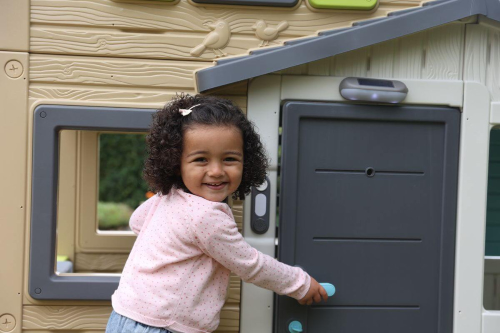 Dziewczynka przed domkiem z dzwonkiem do drzwi smoby