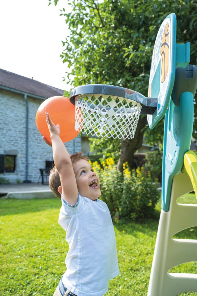 Chłopiec próbująca wrzucić piłkę do kosza do koszykówki smoby zamocowanego na kompatybilnej zjeżdżalni smoby