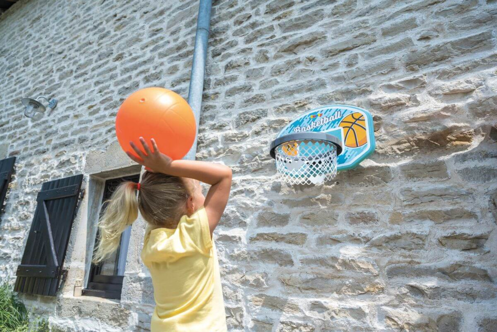 Dziewczynka próbująca wrzucić piłkę do kosza do koszykówki smoby zamocowanego na ścianie domu