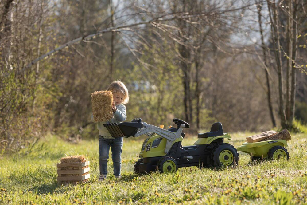 Dziewczynka wrzucająca siano na łyżke traktora farmer max z przyczepką - smoby