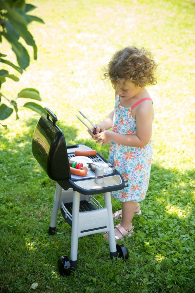 Dziewczynka bawi się obok zestawu do grillowania dla dzieci smoby