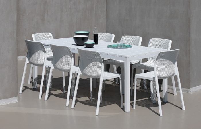 duzy, biały stół z tworzywa sztycznego z 8 krzesłam z ażurowym oparciem ustawiony na nowoczesnym taracie w kolorze szarym