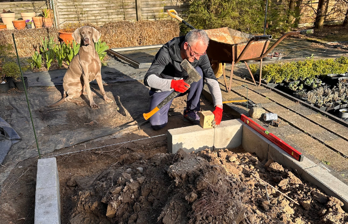 mężczyzna układający fundament pod szklarnię ogrodową na ogórki w ogrodzie 