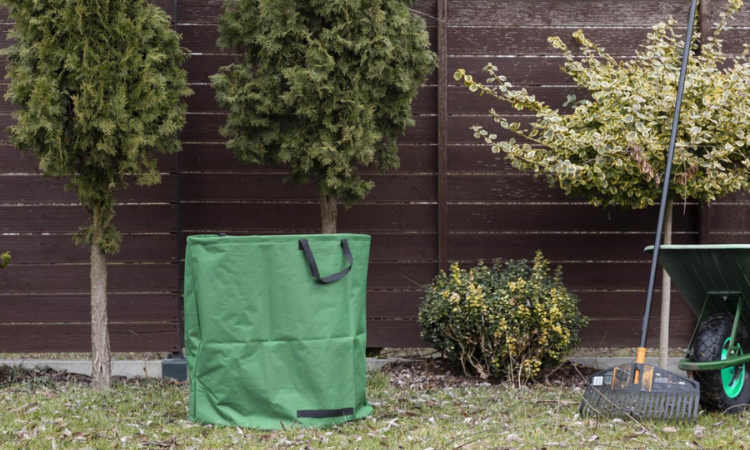 zielony worek na liscie ustawiony w ogrodzie obok narzedzi ogrodowych 
