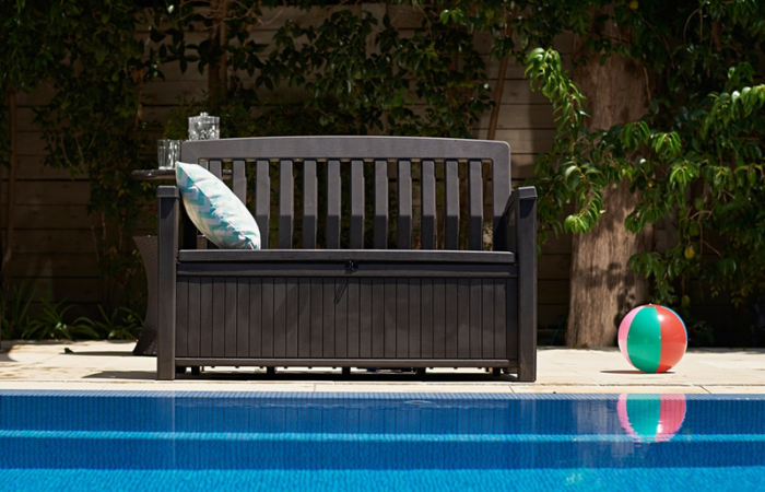 skrzynio-ławka w kolorze brązowym i kolorową poduszką dekoracyjną ustawiona przy basenie w domu 