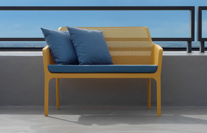 żółta sofa/ławka balkonowa z niebieskimi poduszkami na siedzisku i oparciu ustawiona na balkonie z widokiem na morze 