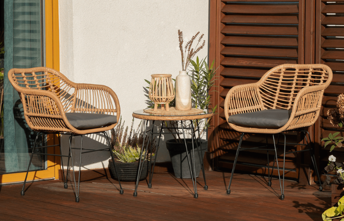 dwa beżowe krzesła z plecionki technorattanowej ze stolikiem ustawione na słonecznym balkonie 