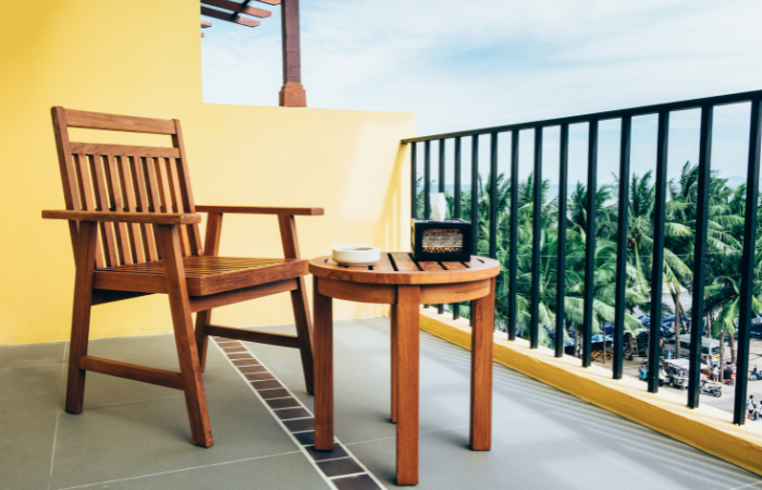 balkon z drewnianym fotelem i stolikiem ze wzorzystymi płytkami 